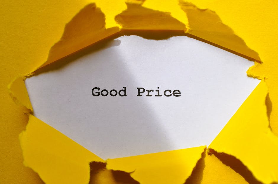 A close-up photograph of a piece of torn yellow paper with rough edges, revealing a white card underneath that displays the text 'Good Price' in black font. The torn paper creates a jagged opening, em